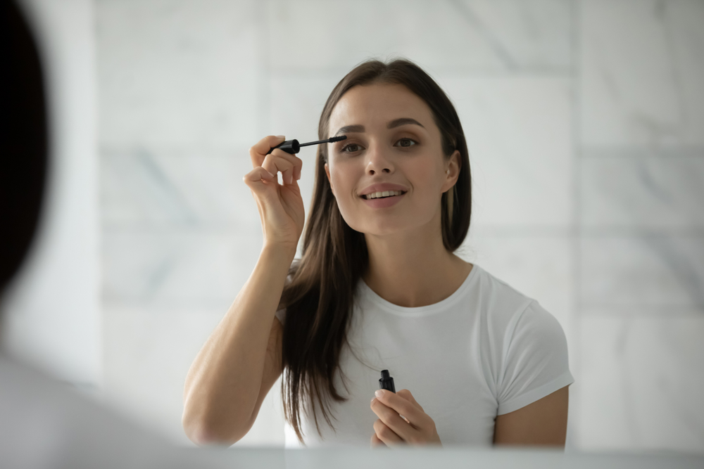 female looking in mirror making herself up using facial decorative cosmetics