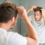 Hair loss man looking in bathroom mirror