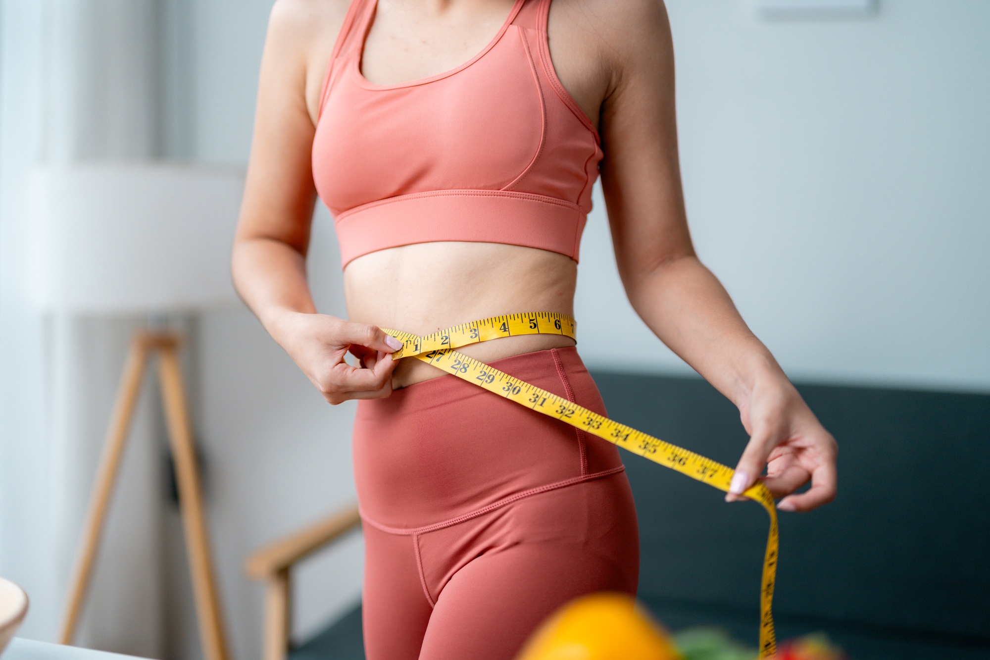 Fit woman measuring her waistline after training, showing progress in her weight loss journey