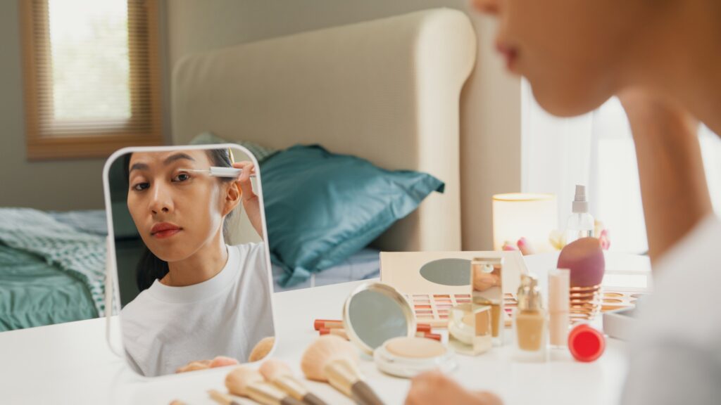 Girl beauty blogger looking at mirror makeup use eye lash mascara top coat serum on eyelash.