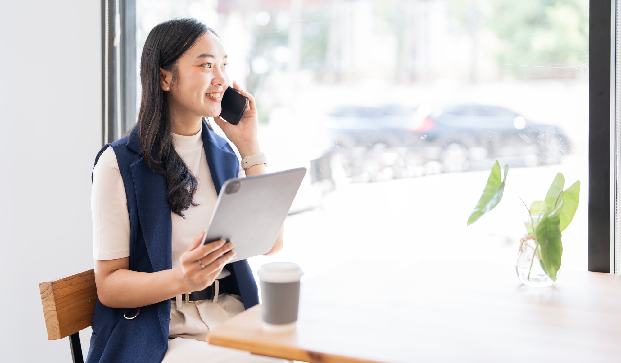Happy asian woman using mobile phone and digital tablet while sitting at cafe.