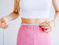 Slim woman measuring her waist's size with tape measure on white background. Successful weight loss
